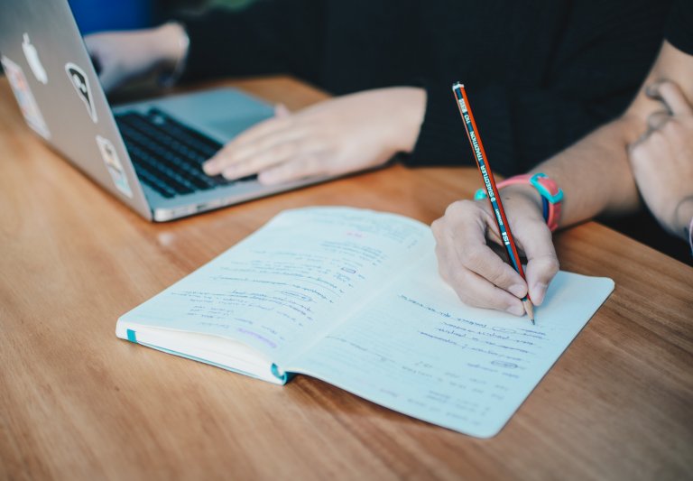 Students writing and working on a laptop