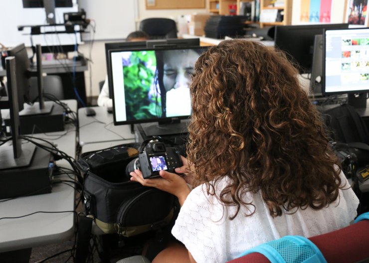 A student sits with a DSLR in front of a computer, working in Saturday Academy’s Digital Photography summer camp 