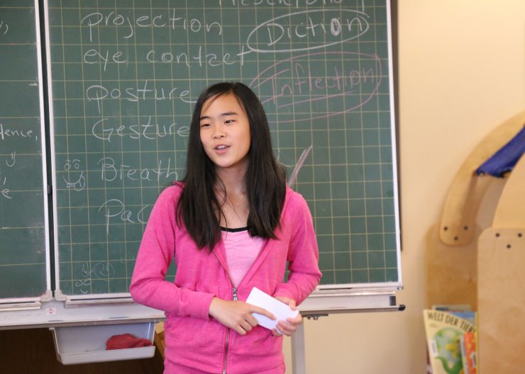 A student stands in front of a chalk board, speaking in Saturday Academy’s Improv summer camp