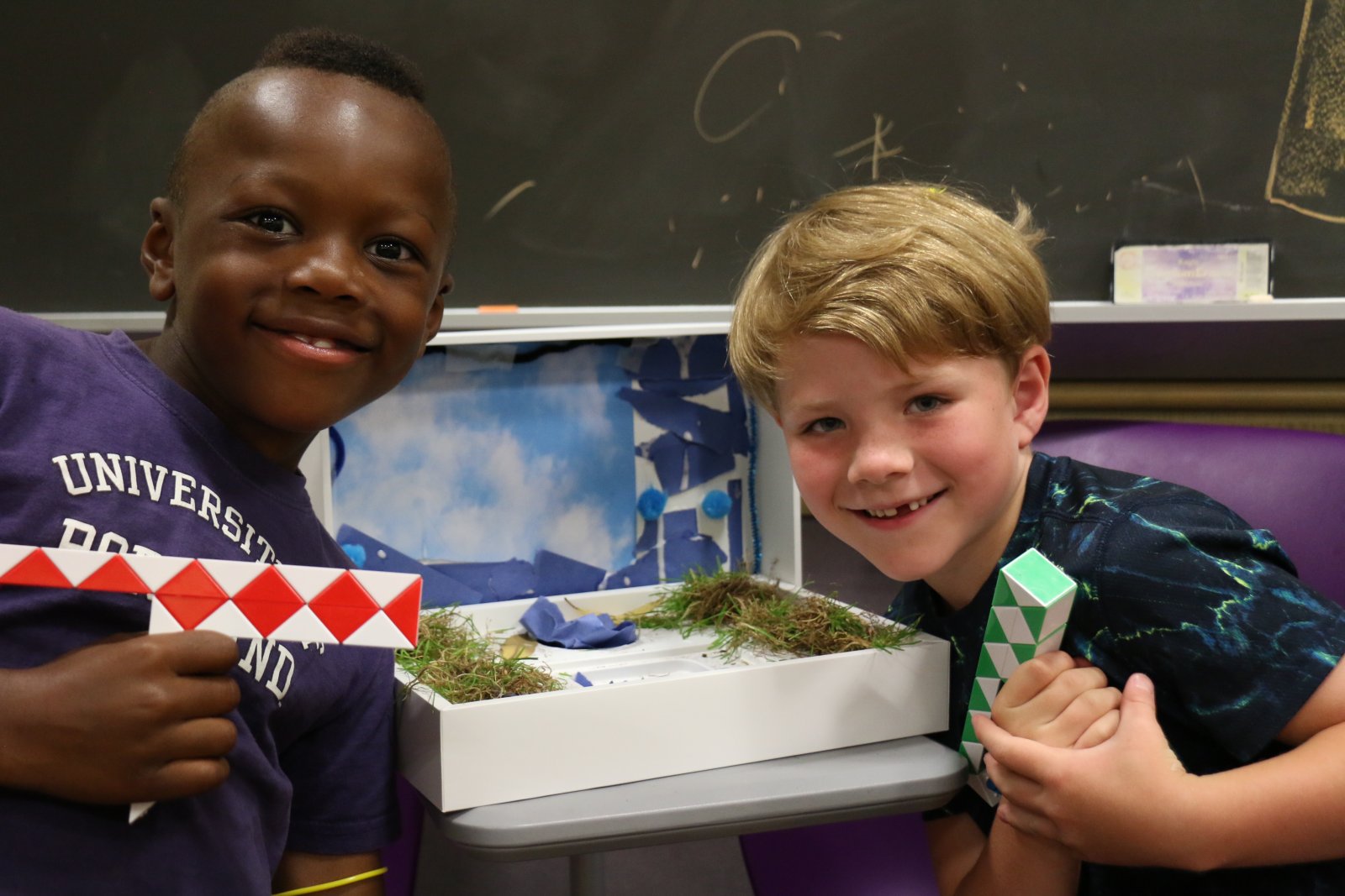 Two kids, white and black, happily showing off their class project