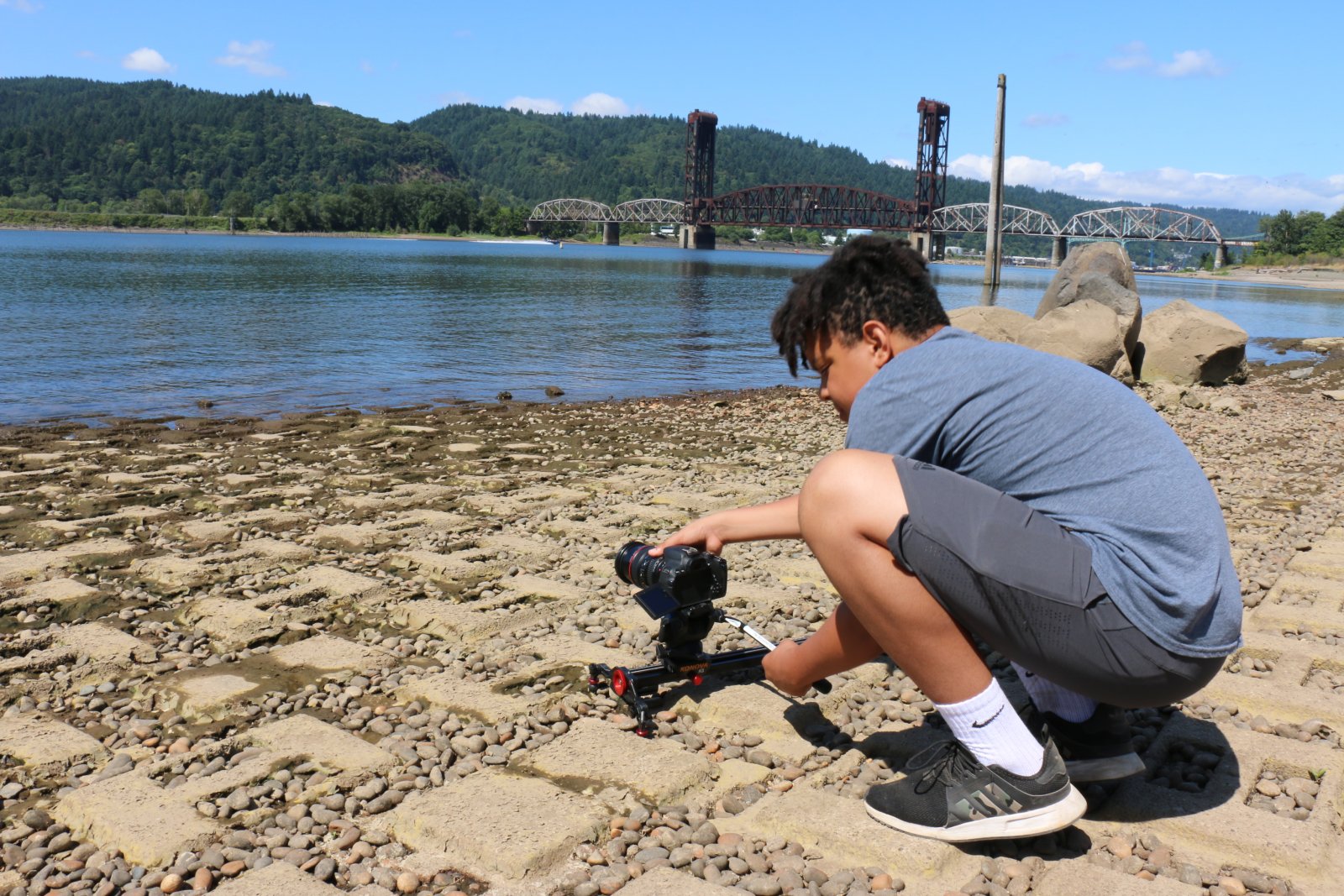 A student, outside on a sunny day, lining up a video camera on the Willamette River in Saturday Academy’s Digital Video Making camp