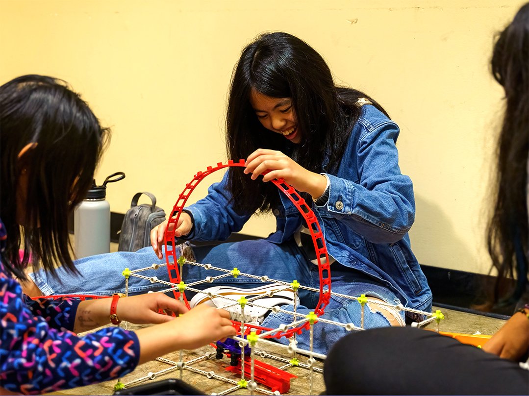 Engineering Three female identifying students work together to construct a rollercoaster