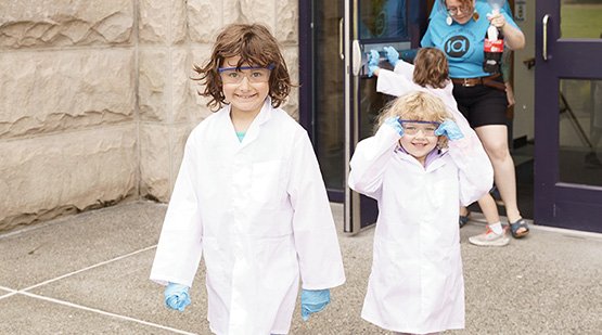 Scientist Explorers Two K-2 summer campers dressed in lab coats and safety glasses on their way to an experiment.